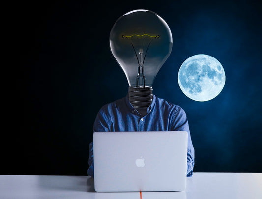 man with lightbulb head using laptop in front of moon